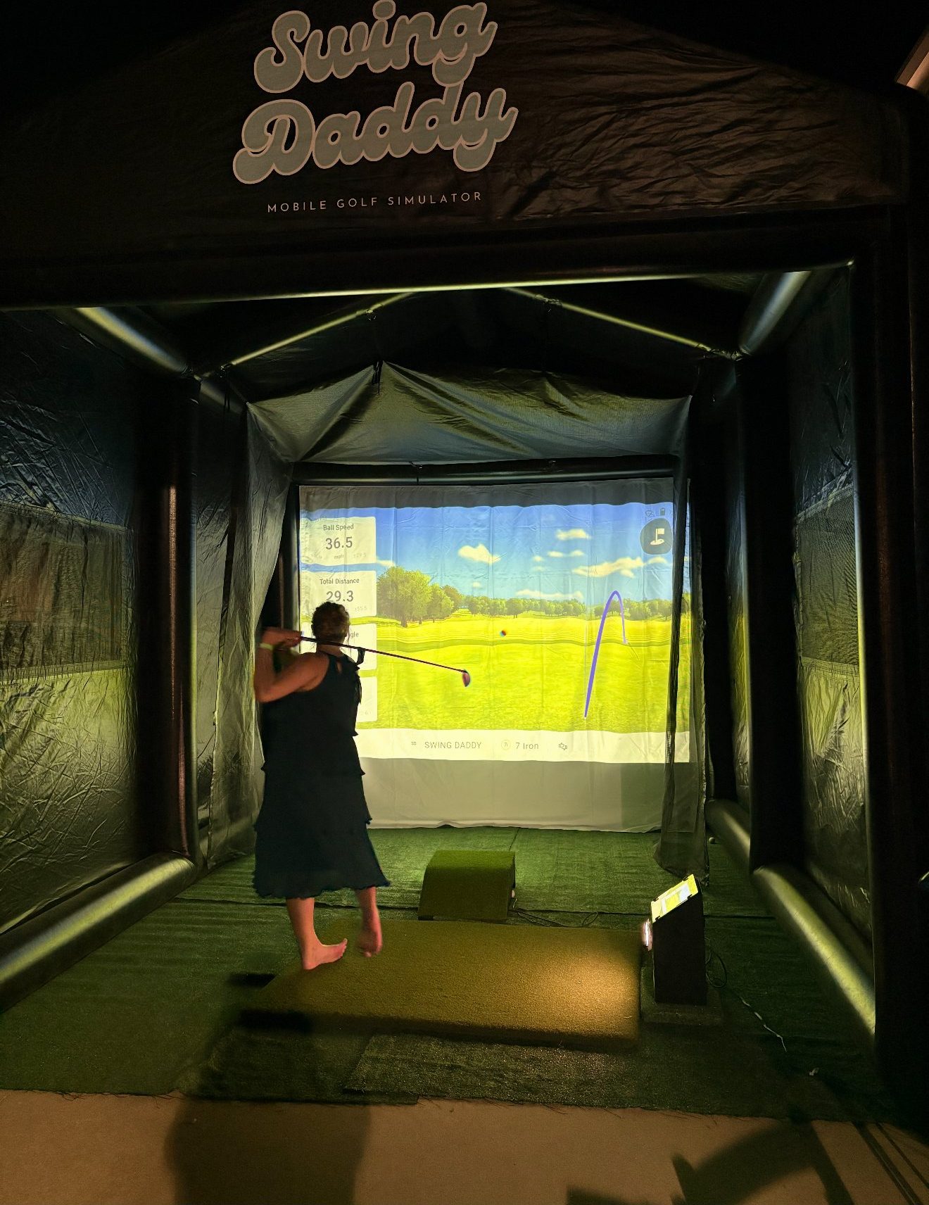 Wedding guest mid-swing inside the branded Swing Daddy golf simulator tent
