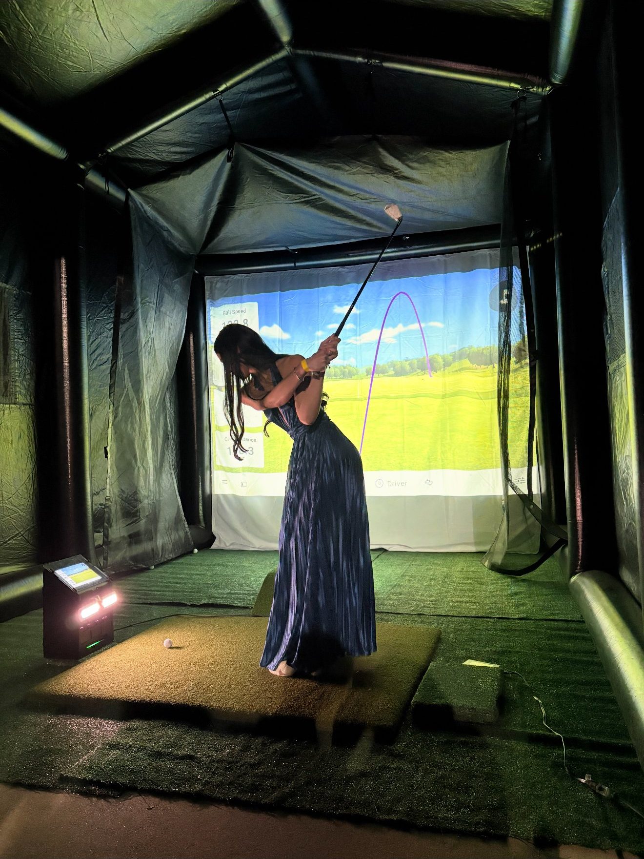 Wedding guest in a formal dress taking a swing inside the Swing Daddy mobile golf simulator